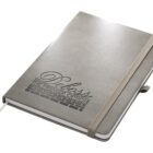 A closed gray notebook with a textured cover. The words Deloss and The Premier Option are embossed on the front. An elastic strap secures the notebook, and a ribbon bookmark peeks out from the bottom.