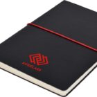 A closed black notebook with a red elastic band and a red logo with the word AUSGLASS on the cover. A black ribbon bookmark extends from the bottom.