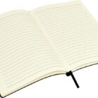 An open notebook with lined cream-colored pages and a black ribbon bookmark lies flat. The notebook has a black cover, and the pages are blank, ready for writing.