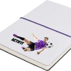 A notebook with a white cover and purple elastic band. The cover features an illustration of a soccer player in a purple jersey kicking a soccer ball. The word ACTIFIT is printed in bold below the image.