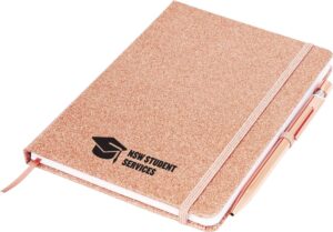 A glittery pink notebook with a pen attached. The cover has a logo featuring a graduation cap and the text NSW Student Services in black.