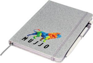 A closed gray notebook with a colorful geometric lion design and the word MUJJO on the cover. A pen is tucked into the notebooks elastic band.