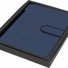A closed blue journal with a snap closure is placed inside a black box. The box has a snug fit, showcasing the journals textured cover. The journal is centered, and the background is white.