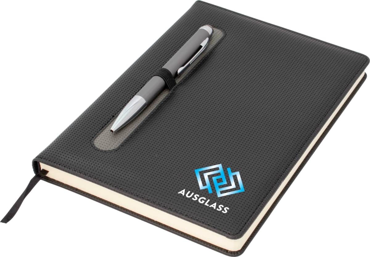 A black notebook with a pen holder integrated into the front cover, holding a silver pen. The cover features a blue and white geometric logo and the text AUSGLASS. A black bookmark ribbon is visible.