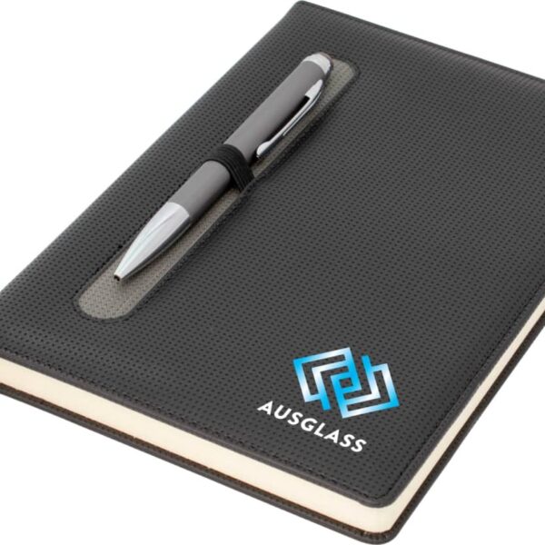 A black textured notebook with a sleek silver pen attached in a dedicated slot. The cover features a blue geometric logo and the word AUSGLASS. A black ribbon bookmark is visible.