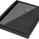 A gray and black fabric-covered planner or journal in a black box. The planner has a diagonal design with stitched accents and a gray fabric loop, giving it a sleek, modern look.