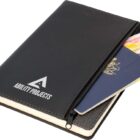 A black zippered notebook with Ability Projects on the cover. A passport, currency notes, and a small notebook are partially visible inside the front pocket.