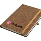 A brown notebook with a cork-textured cover features the Instagram logo and name. It has an elastic band for closure and a ribbon bookmark.