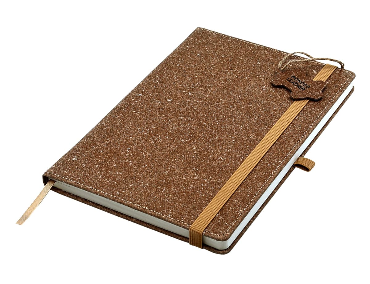 A brown textured notebook with a ribbon bookmark and elastic band closure. A tag is attached to the band on the top right. The cover has a natural, speckled appearance.