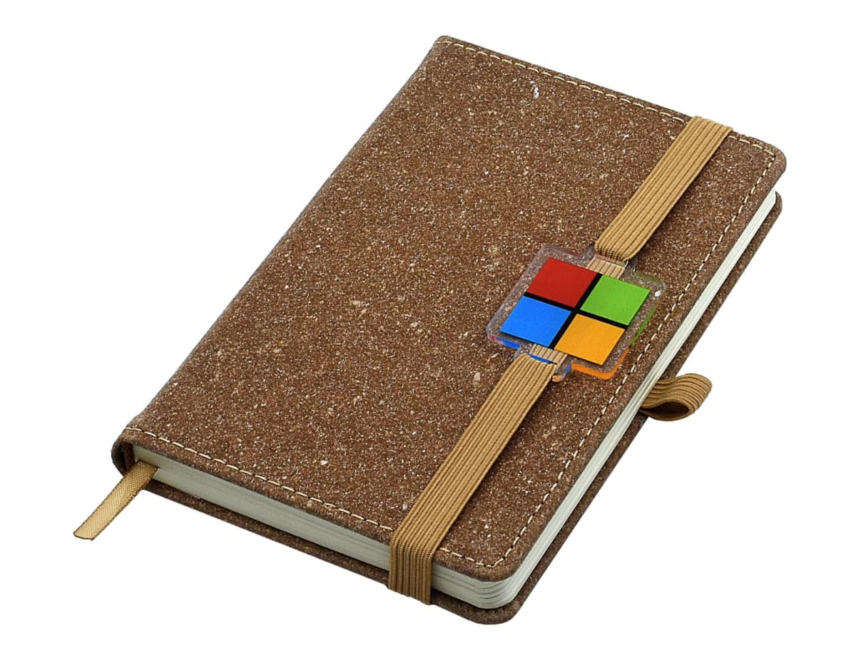 A brown speckled notebook with an elastic strap, featuring a colorful square logo near the strap. The notebook is closed and appears to have a bookmark ribbon.