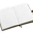 An open notebook with lined pages and spaces for dates at the top. A brown ribbon is placed between the pages as a bookmark. The notebook has a brown cover.