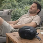 Man relaxing on a patio with Kairo Outdoor Bluetooth Speakers and water on the table.