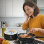 Woman in yellow sweater cooks veggies near Nair Bluetooth Speakers in a bright kitchen.