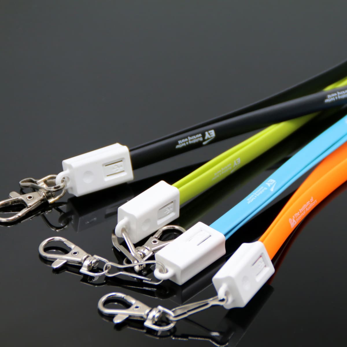 Close-up of several colorful lanyards with metal clips and white attachment clasps on a glossy black surface. The lanyards are black, green, yellow, blue, and orange.