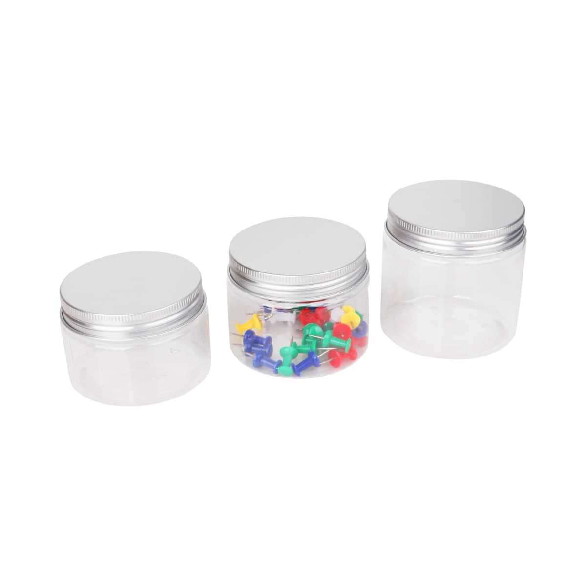 Three transparent jars with silver lids. The first jar is empty, the second contains colorful push pins, and the third is empty. The jars are arranged in a row on a white background.