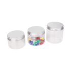 Three transparent jars with silver lids are lined up. The left jar is empty, the middle jar contains colorful push pins, and the right jar is also empty.