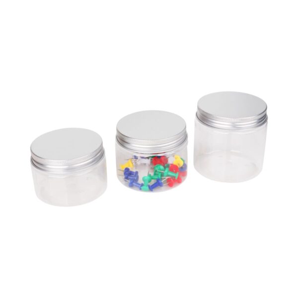Three transparent jars with silver lids are lined up. The left jar is empty, the middle jar contains colorful push pins, and the right jar is also empty.