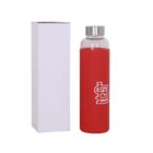 A red glass water bottle with a metal cap and a white logo, featuring interlocking letters, stands next to a plain white box.