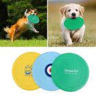 Two dogs play with green frisbees; a Shetland Sheepdog leaps in a field, and a Golden Retriever puppy sits with a frisbee in its mouth. Below, three frisbees are displayed: yellow with a design, blue with a target, and green with the Simparica logo.