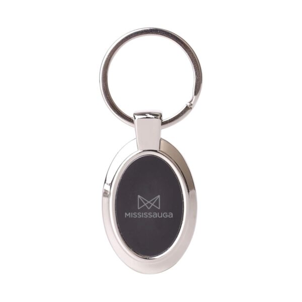 A metal keychain featuring an oval black center with the text Mississauga and a minimalist logo printed on it. The keyring is attached at the top.