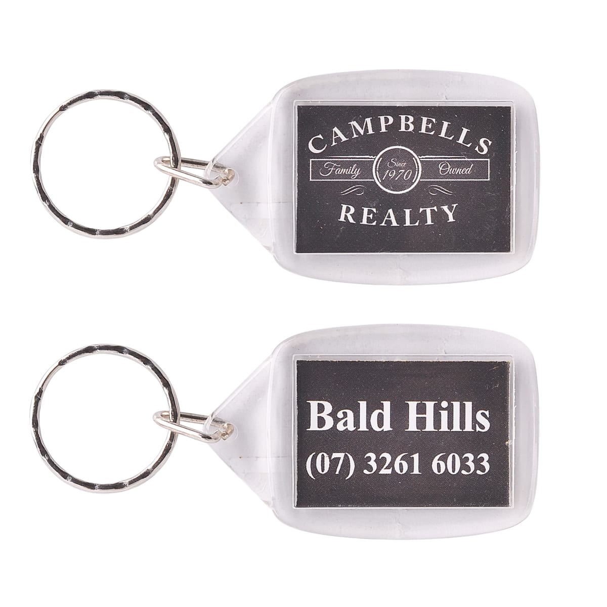 Two keychains with clear plastic frames. One keychain reads CAMPELLS REALTY, Family Owned Since 1970 and the other says Bald Hills, (07) 3261 6033. Both have metal rings attached.