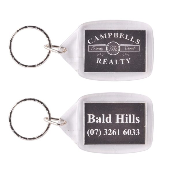 Two rectangular keychains with silver rings. The first reads Campbells Realty, Family Owned Since 1970. The second says Bald Hills followed by the phone number (07) 3261 6033. Both have a black background with white text.