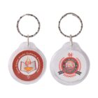 Two round keychains with metal rings. The left keychain features the Gold Coast Hindu Cultural Association logo with a lamp design. The right keychain displays the Moorabbin Cricket Clubs 100th games emblem with red and black accents.