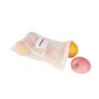 A reusable mesh bag containing an orange and a partially visible apple is placed on a white surface. Next to the bag, there is a pink apple. A small white label with blue text is attached to the bag.