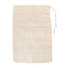 A plain, beige drawstring bag with the word Victoria printed in white on the front. The bag is laid flat against a white background, and the drawstring is tied in a knot at the top right corner.