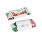 Two reusable food pouches wrapped in colorful fabric adorned with vegetables and citrus illustrations. One is placed flat, and the other is partially unfolded, revealing a white inner lining with a brand logo.