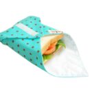 A sandwich with lettuce and tomato is wrapped in a teal fabric with brown polka dots. The wrap has a white interior and is slightly open, revealing part of the sandwich.