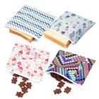 Four reusable fabric sandwich bags with various colorful patterns. Two bags contain bread slices, while two bags have animal-shaped cookies spilling out. Patterns include zigzags, cacti, cupcakes, and geometric shapes.