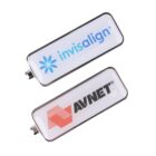 Two rectangular USB flash drives placed side by side. The top drive has a logo and the word invisalign in blue. The bottom drive has a red striped logo and the word AVNET in black. Both have a shiny, metallic rim.