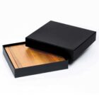 A black, square gift box with a removable lid. Inside, a flat wooden panel is visible. The box is placed on a white background.
