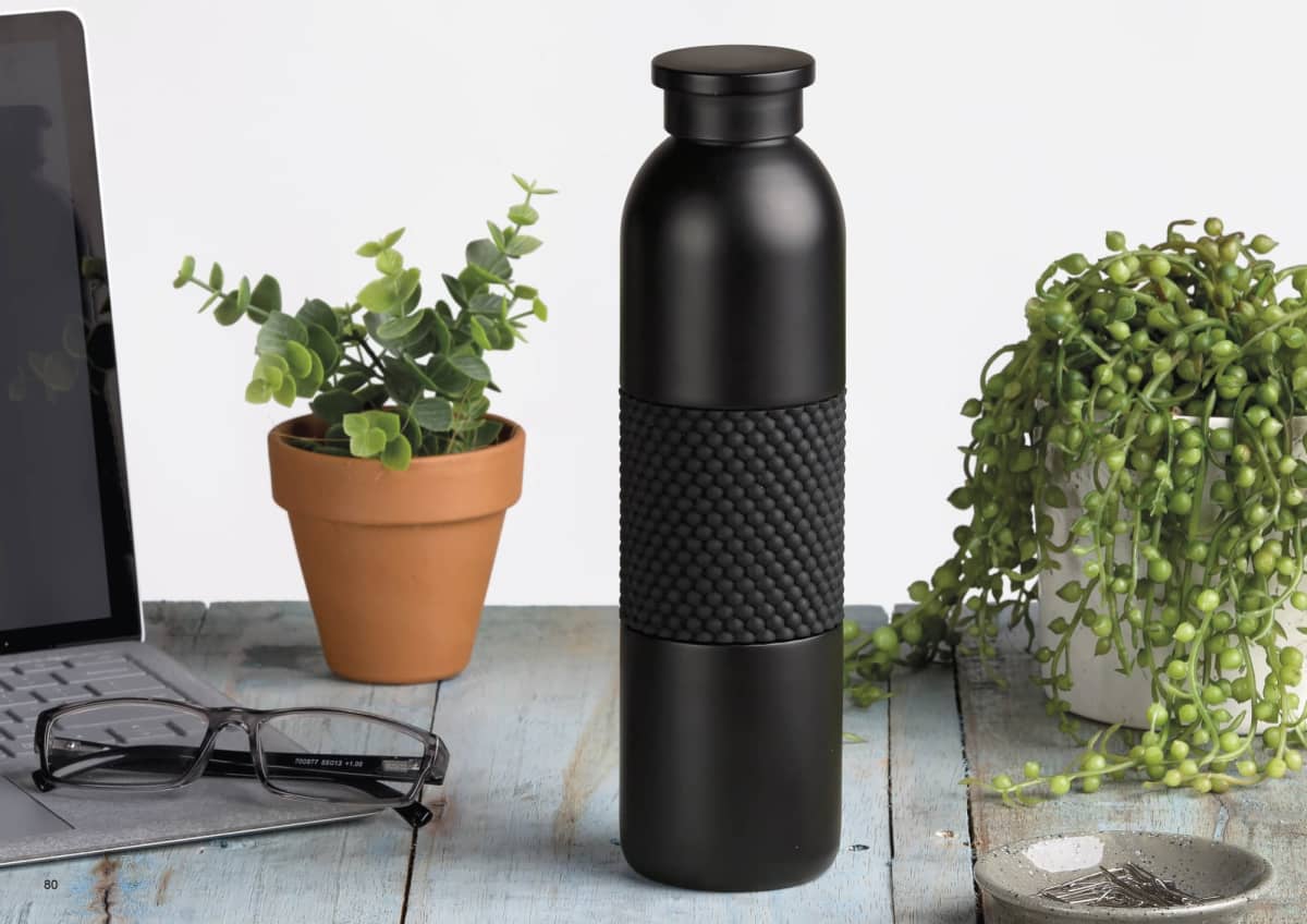 A sleek black water bottle with a textured grip sits on a wooden table surrounded by a laptop, eyeglasses, and small potted plants.