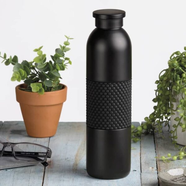 A sleek black water bottle with a textured grip sits on a rustic wooden table, surrounded by a laptop, a pair of glasses, and two small potted plants.