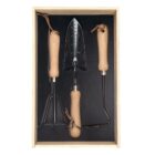 A wooden box containing three gardening tools with wooden handles: a trowel, a hand rake, and a weeder. They are neatly arranged against a black background.