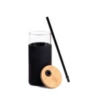 A sleek, modern drinking glass with a black silicone sleeve and a bamboo lid is shown. A long black straw leans against the glass. The design is contemporary and minimalist.