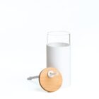 A minimalist bathroom toilet brush set featuring a white cylindrical holder with an open top and a wooden lid, placed against a plain white background. The brush handle is visible beside the holder.