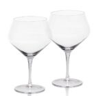 Two clear, empty wine glasses with long stems and wide bowls are placed side by side against a plain white background.