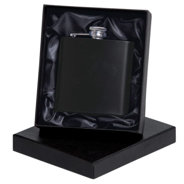 A sleek black flask is presented in an open black gift box with a silk lining. The flask has a shiny cap, and the box is slightly tilted to display both the flask and its elegant packaging.