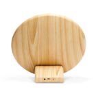 A round, wooden object with a smooth, natural grain pattern sits on a rectangular wooden base. The base has a small button and port, suggesting functionality. The design is minimalist and modern, with a light wood finish.