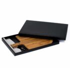A wooden cutting board partially slid out from a black rectangular box. A white cylindrical object is also visible in the box, next to the cutting board.