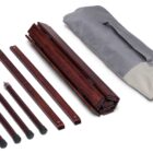 A collection of disassembled dark wooden rods and planks lies next to a gray storage bag. The rods have metal tips, and the bag is partially open with drawstrings. The wooden pieces appear to be parts of a furniture or structure kit.