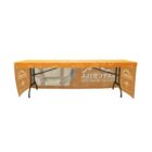 A long, rectangular table is covered with an orange tablecloth printed with YETI CHILL. A cooler with a shoulder strap is visible in the center. The table has a metal frame and the floor is white.