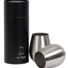 A black cylindrical box with text stands beside two sleek, silver, stemless wine glasses placed at different angles.