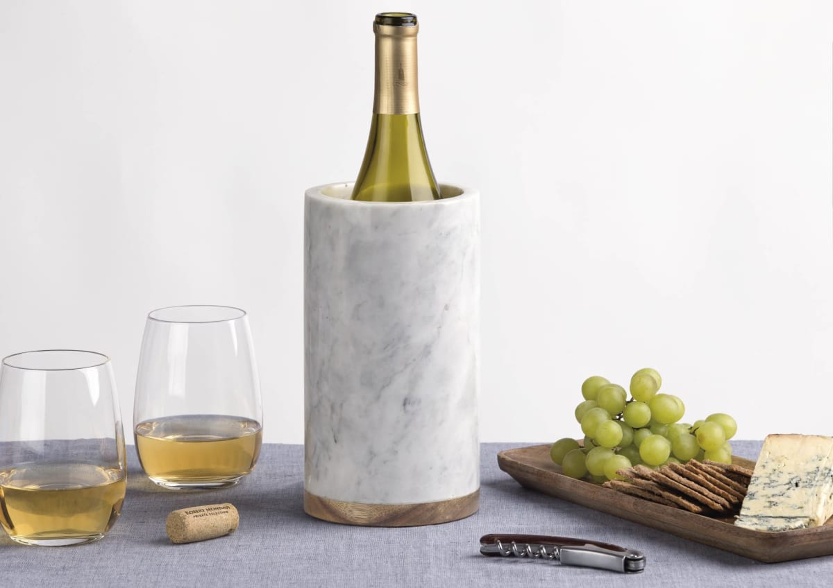 A marble wine cooler holds a bottle of wine, with two filled glasses nearby. A wooden tray displays green grapes, crackers, and cheese. A corkscrew and cork rest on a gray tablecloth, creating an elegant scene.