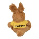 Brown plush bunny sitting with its back facing forward, wearing a yellow shirt with the text medeco on it.