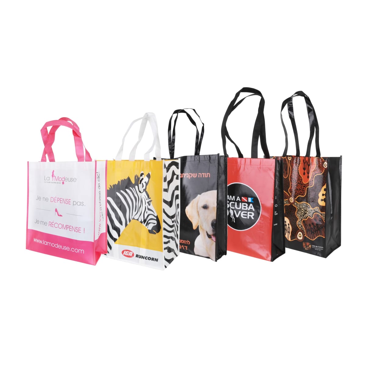 Five colorful tote bags with different designs stand upright. From left to right: pink with text, zebra photo, dog photo, scuba diver logo, and abstract design. Each bag has long handles.