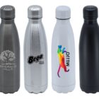 Four stainless steel water bottles are displayed. Each bottle has a different design: a tree logo, Bega text, a colorful geometric animal, and a plain black bottle. They are arranged in a row on a white background.